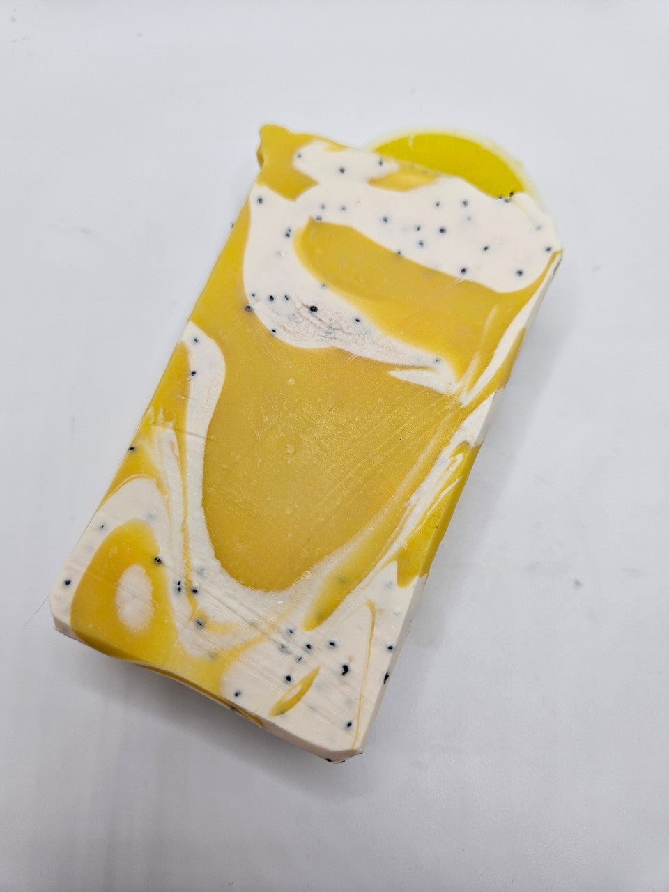 Artisan soap bar with a yellow lemon center, white swirls, and scattered black speckles