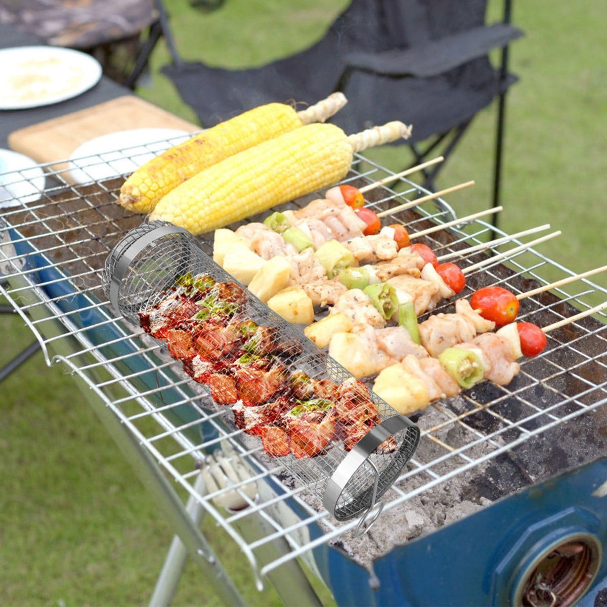 Two cylindrical mesh grill baskets on a camping grill, holding corn and diced meat
