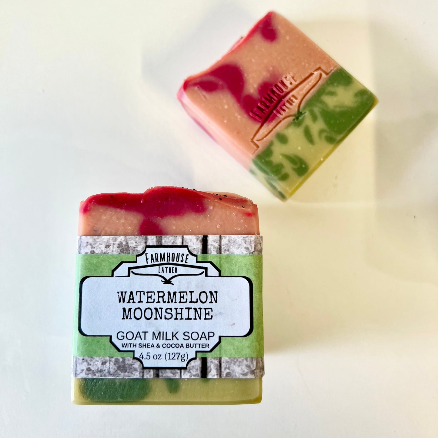 Goat milk soap bar labeled Farmhouse Watermelon Moonshine, green base and pink top