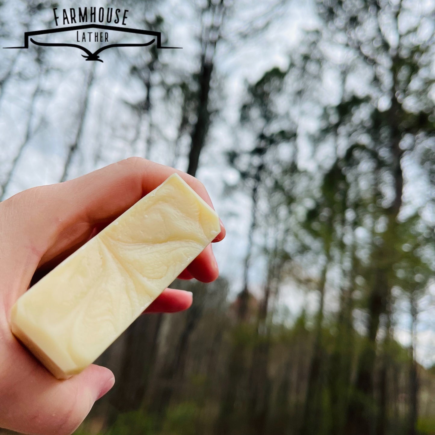 Unscented soap bar, pale cream rectangular block held in hand outdoors