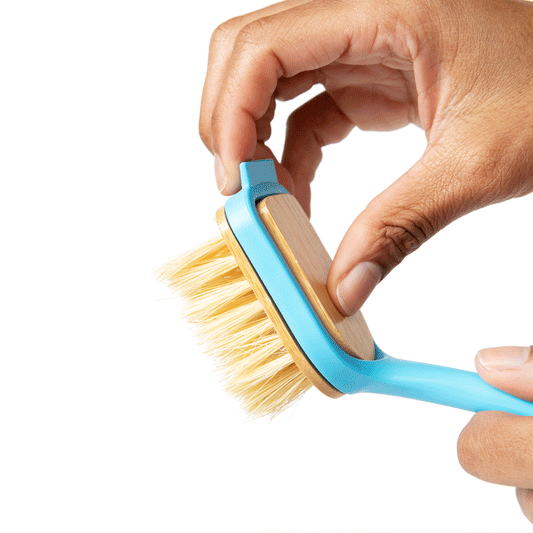 Hand holding a blue dish brush with tan wooden head and light bristles