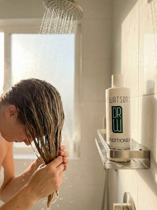 Dr. Watson's conditioner bottle in shower holder, with person rinsing wet hair