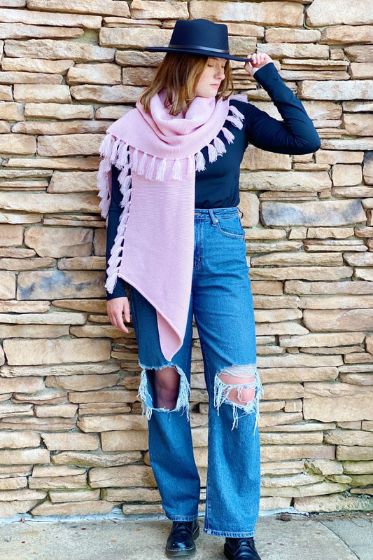 Pink fringed knit blanket scarf, draped over shoulders with ends hanging