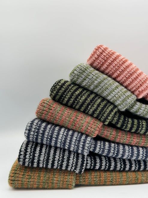 Cuffed knit beanies stack in green, black, blue, and rust with patterned stripes