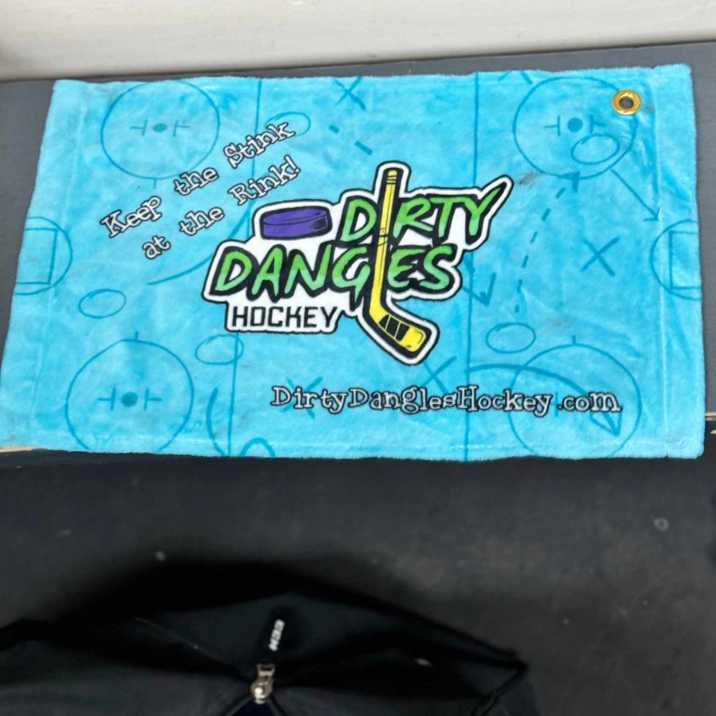 Sky-blue towel panel with Dirty Dangles Hockey logo and website text, grommet