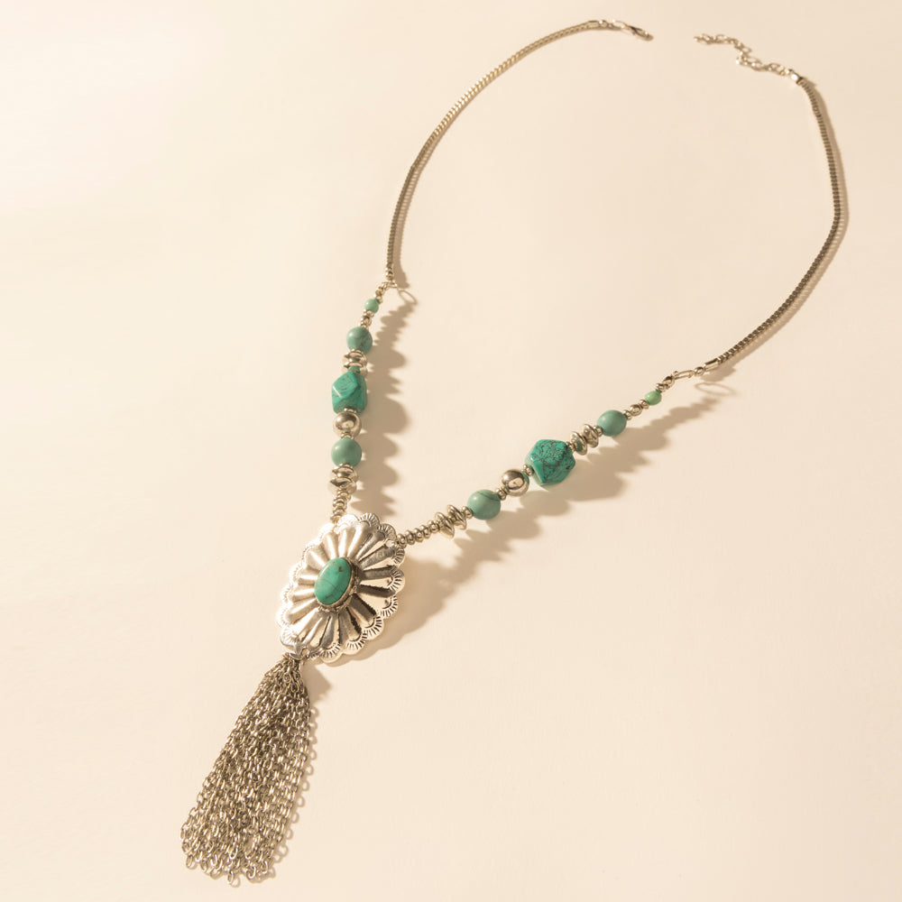 Pendant necklace with turquoise green beads, silver sunburst charm, and tassel