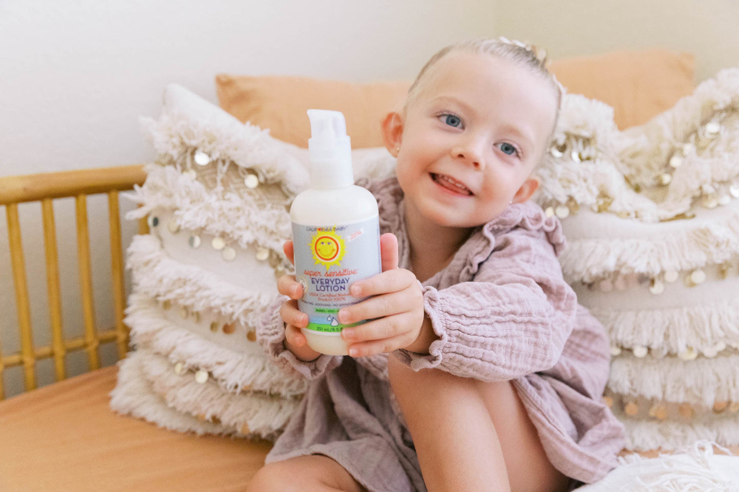 Baby holding a hands kit lotion bottle on a cushioned chair