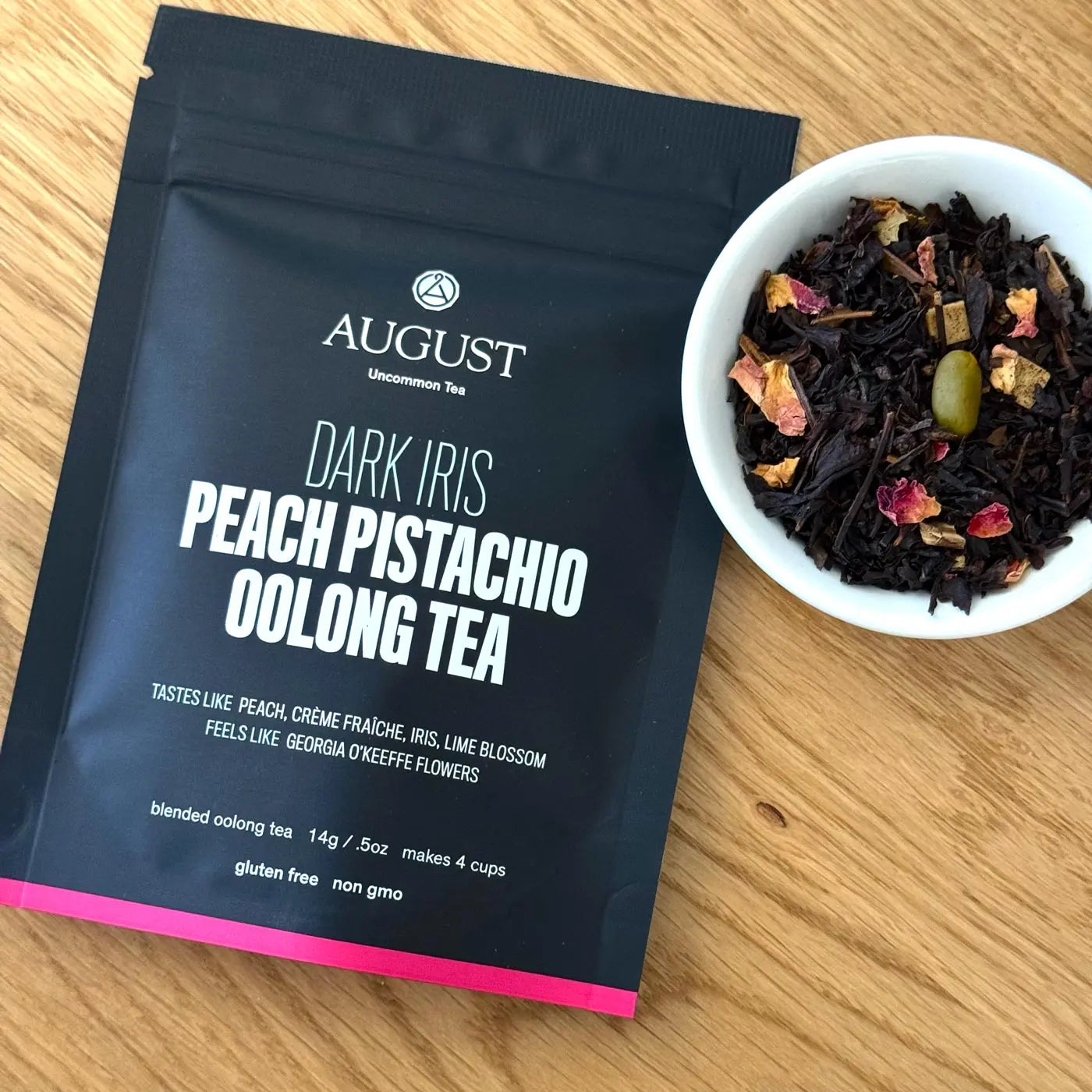 Dark tea pouch with AUGUST branding and a bowl of dried tea leaves; peach bits