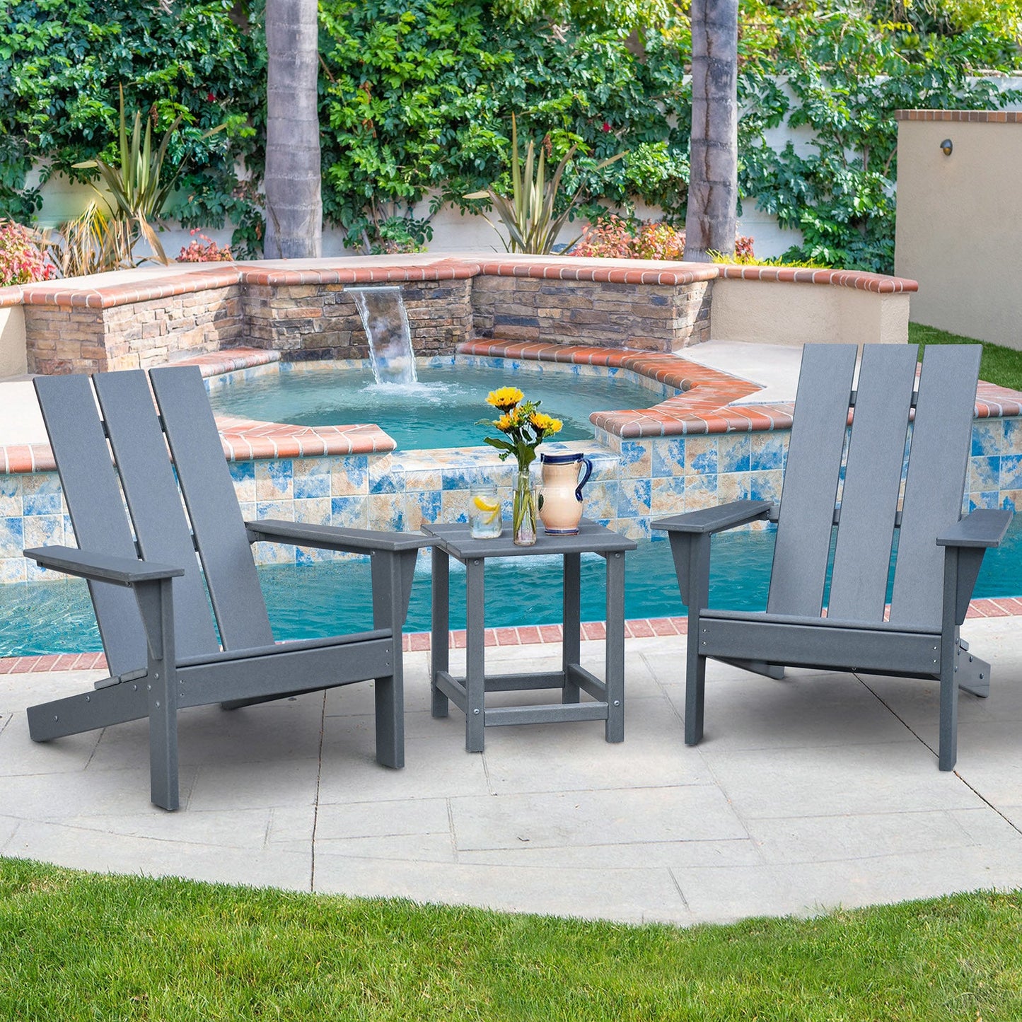Dark grey outdoor Adirondack chairs with matching side table beside a swimming pool