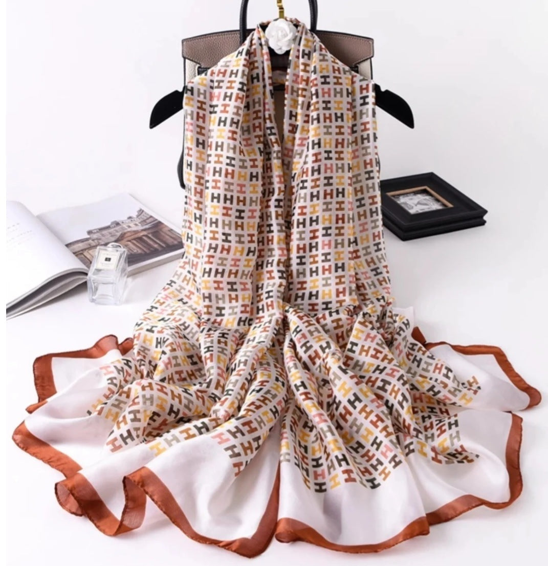 Luxury silky scarf with white base, repeating H monogram print and rust border edges