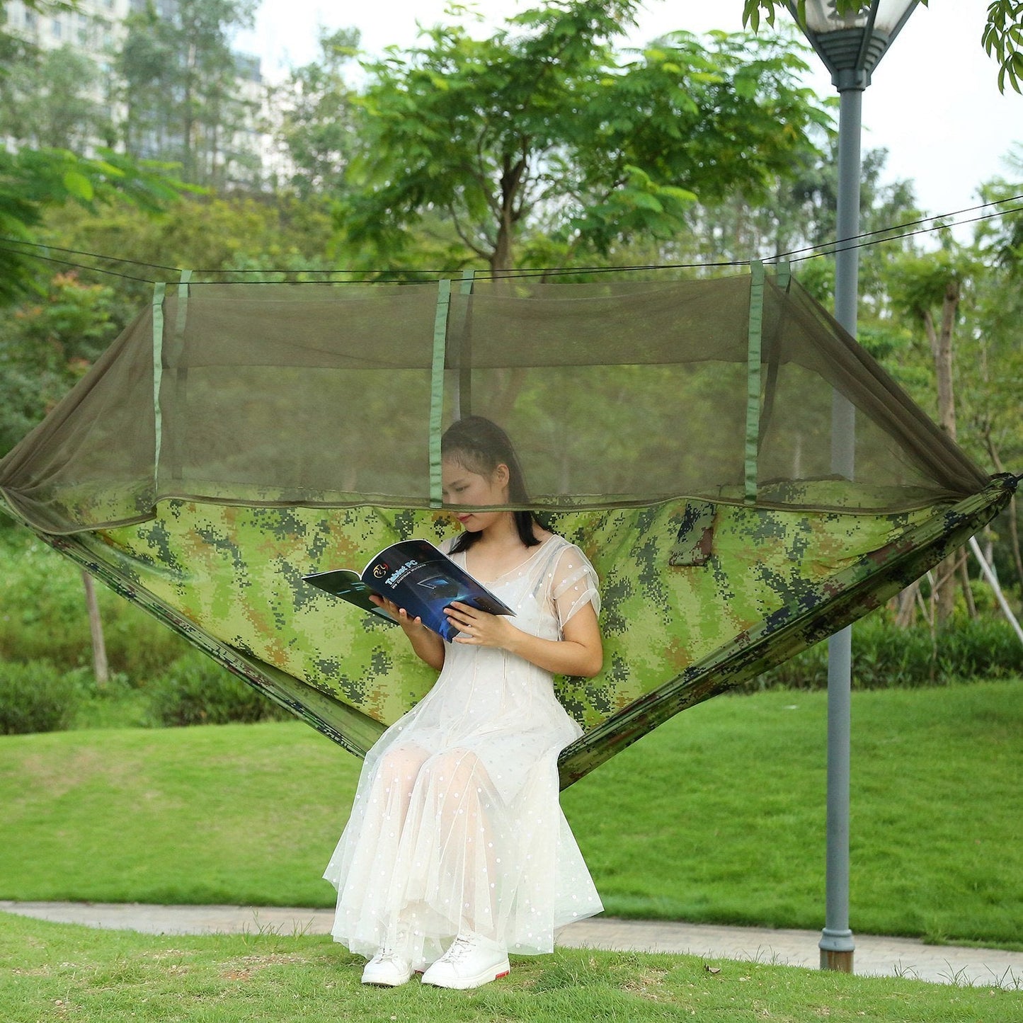 Two-person camo hammock with mosquito net, person relaxing outdoors on grass