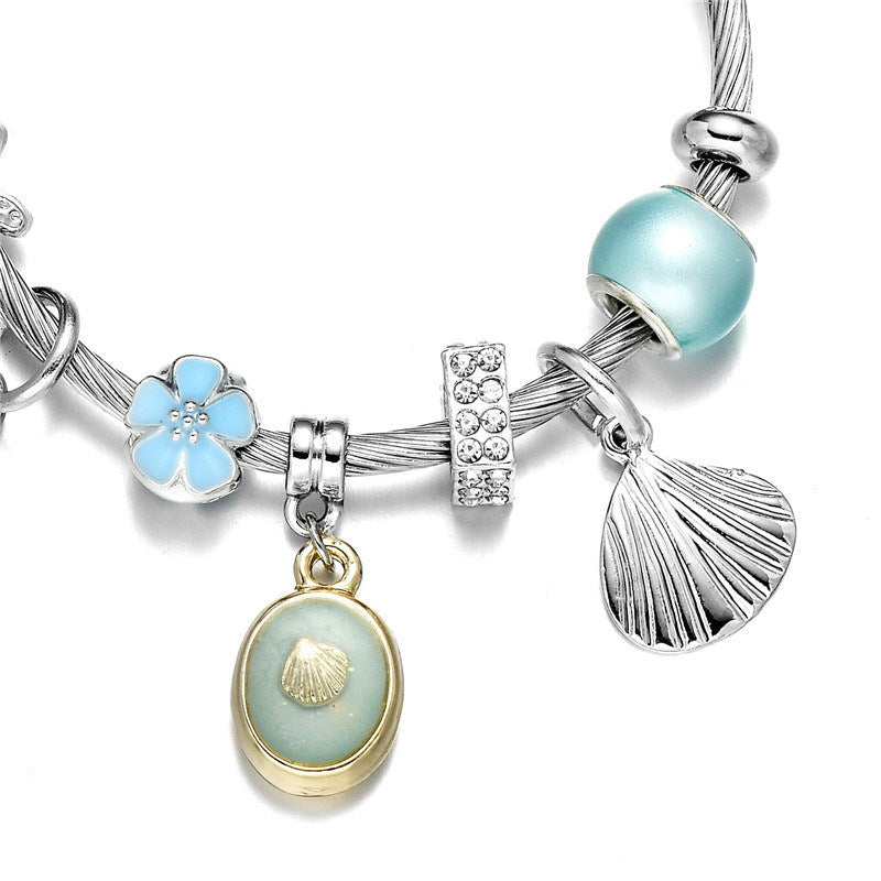 Silver wrap bangle bracelet detail with blue bead, flower charm and oval shell pendant