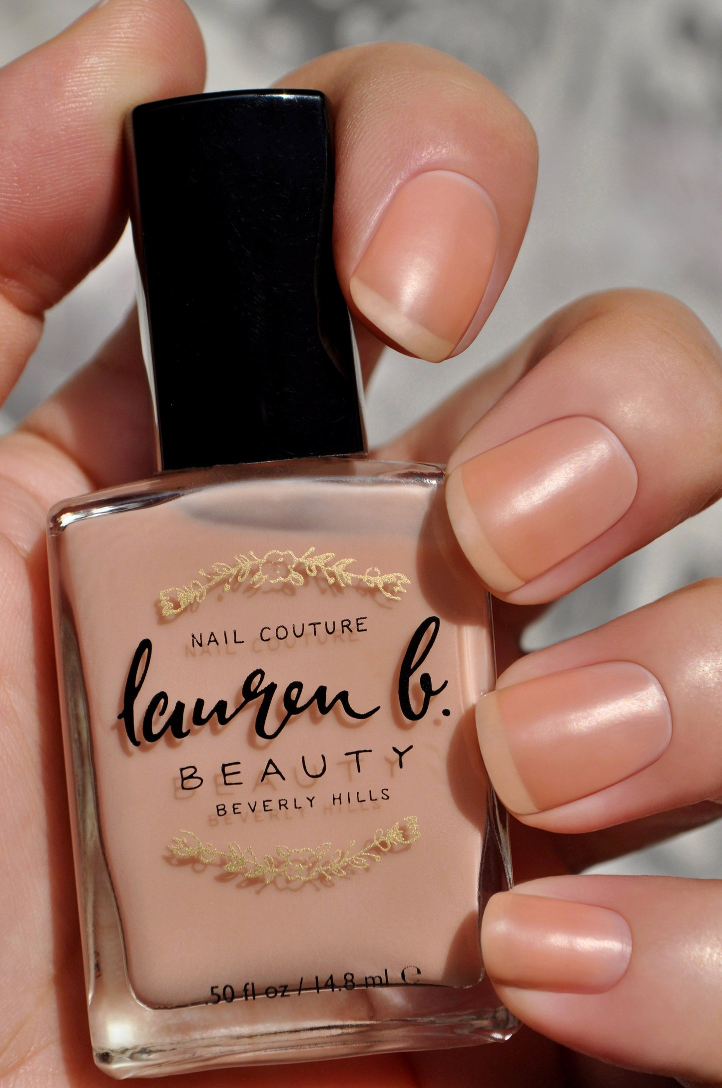 Nail base coat bottle in a nude peach shade held by fingers.