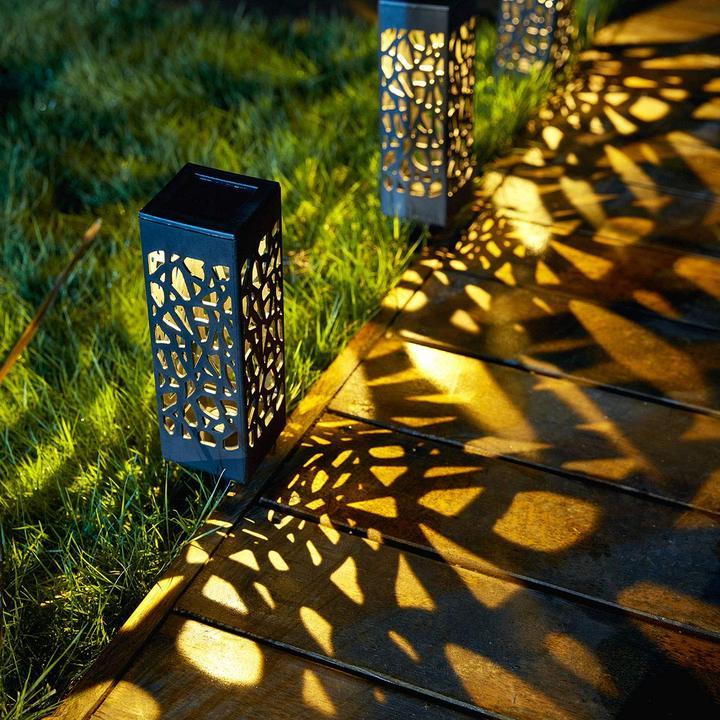 Black solar garden light with cutout pattern glowing in grass