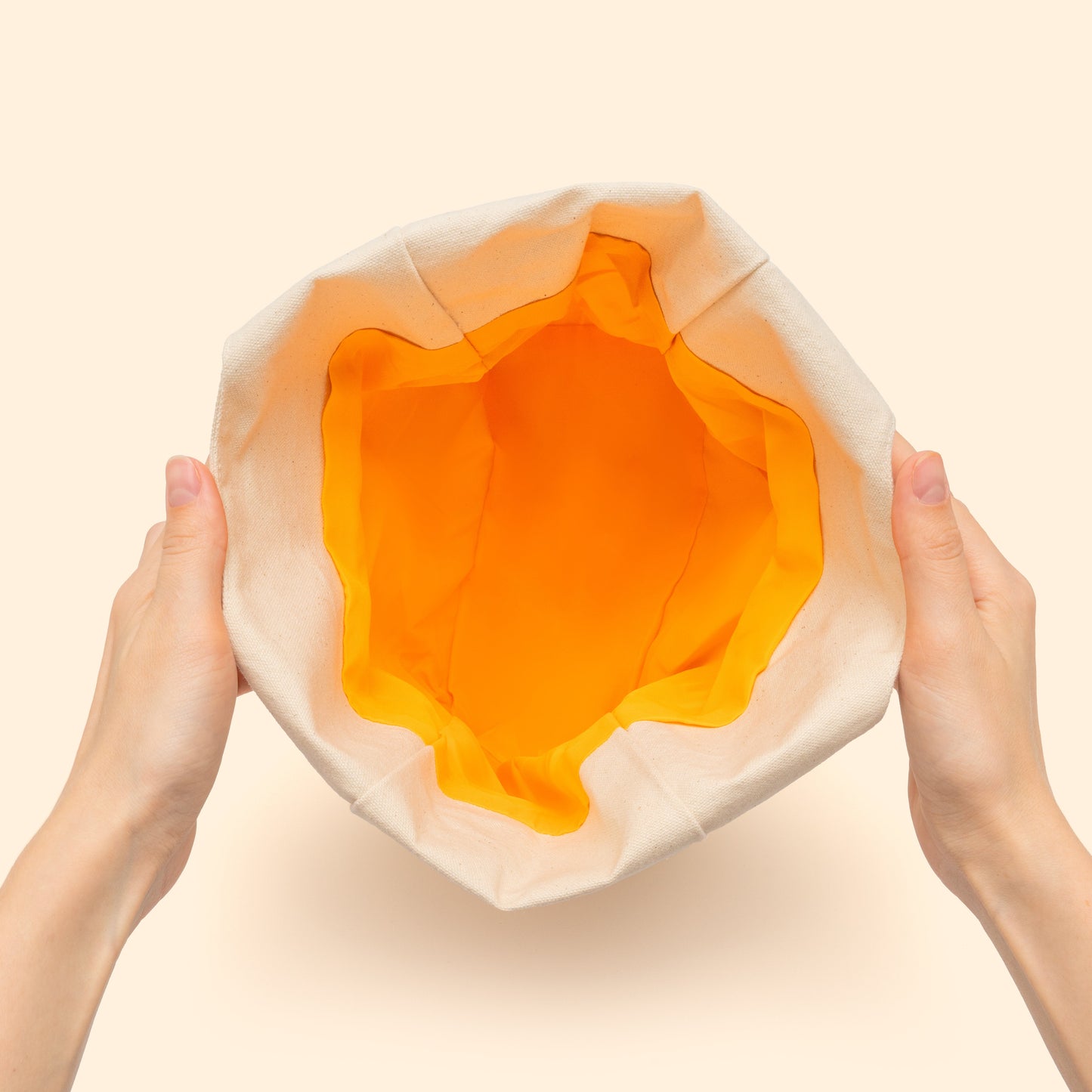 Light-beige canvas basket opened, showing orange fabric lining and inner folds