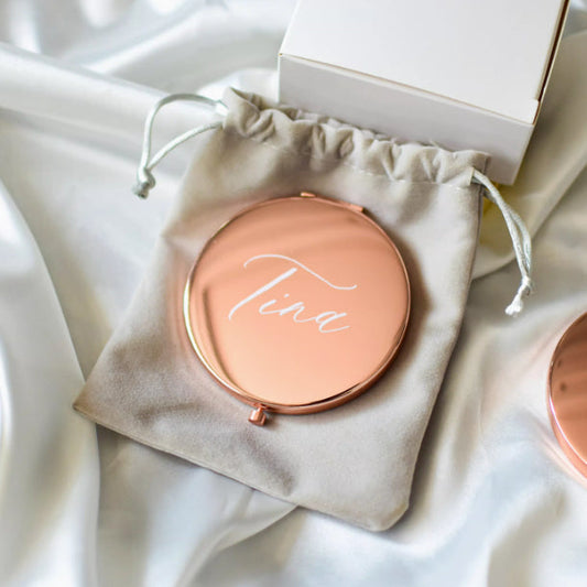 Rose gold personalized compact makeup mirror with cursive name, in drawstring gift pouch.