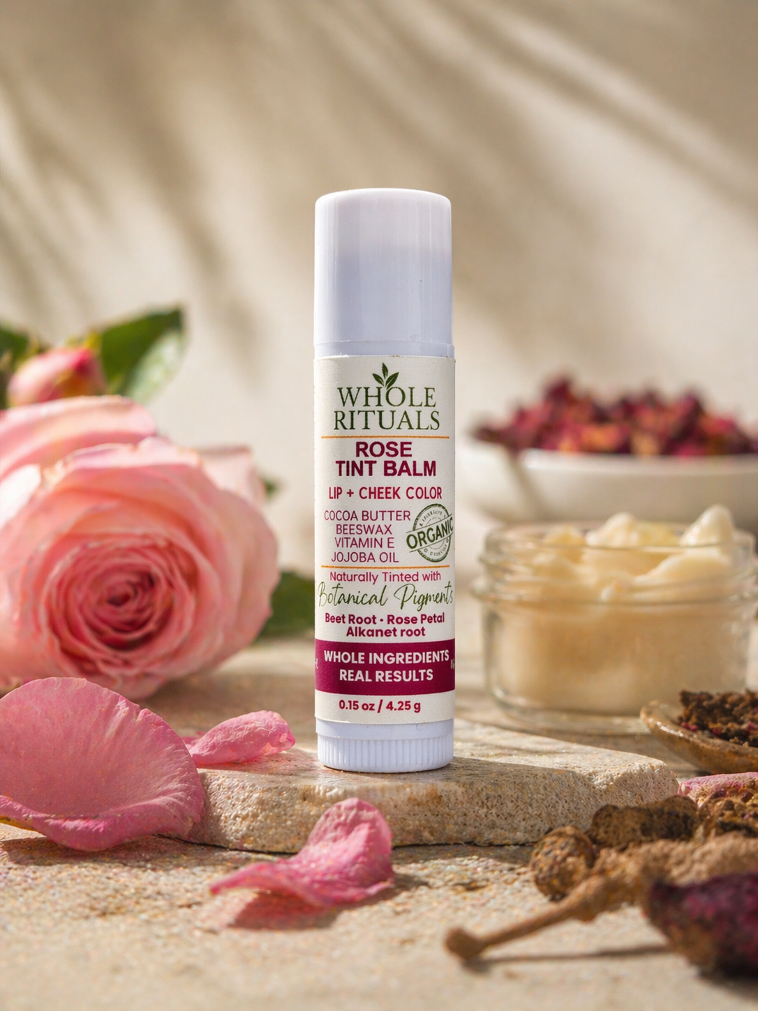 Rose tint balm stick on a stone surface with pink rose petals, for lips and cheeks