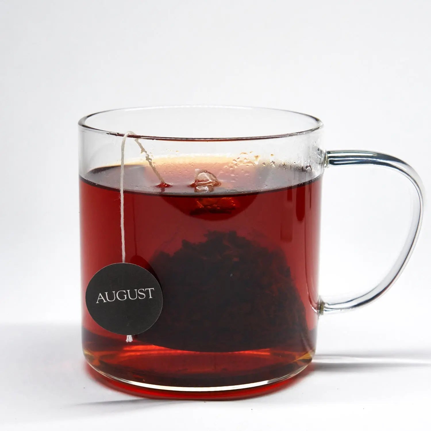 Glass cup of dark tea with a visible tea bag string and label seal