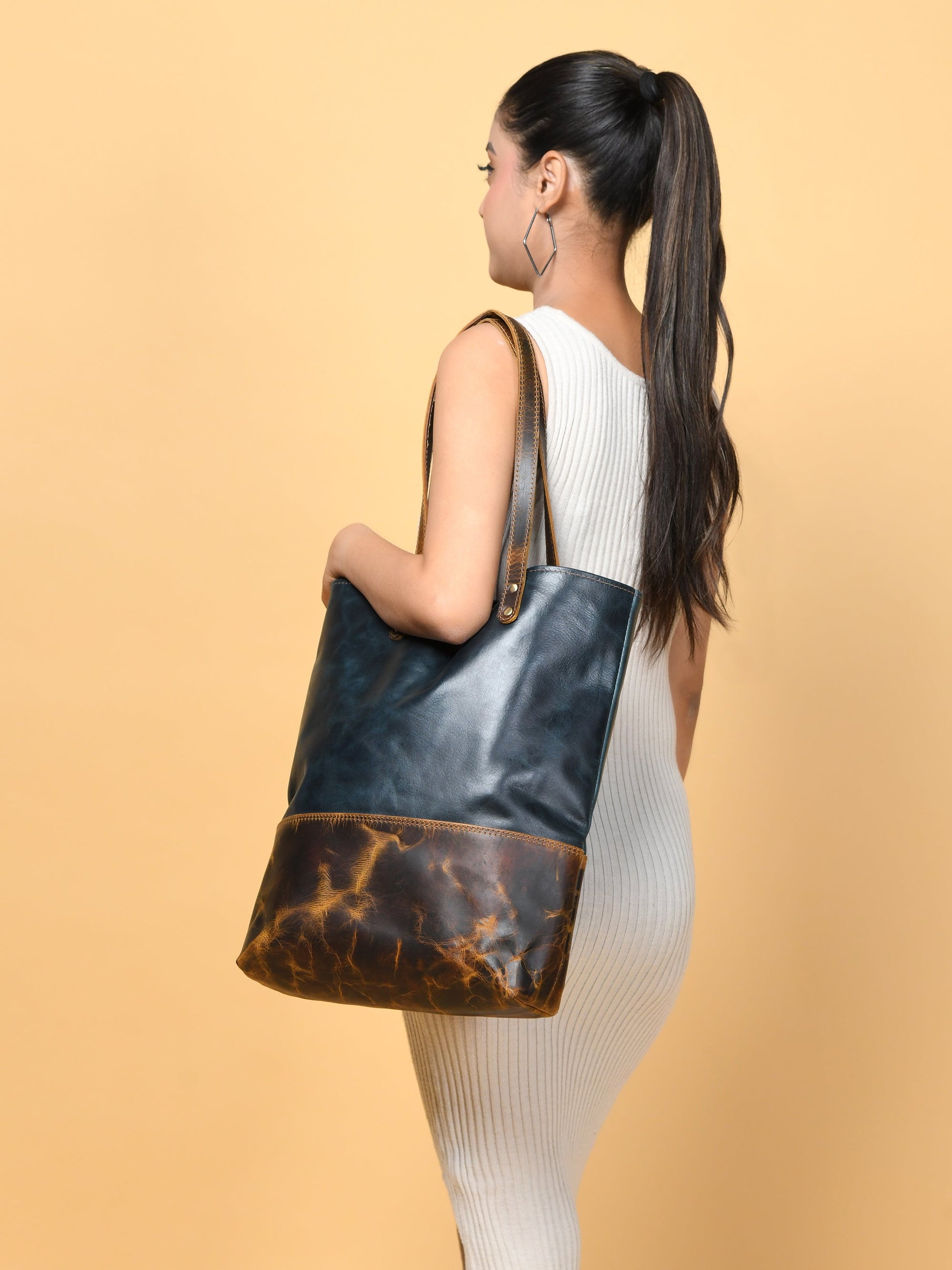 Dark blue leather tote with tan-brown bottom panel, carried by a woman in profile