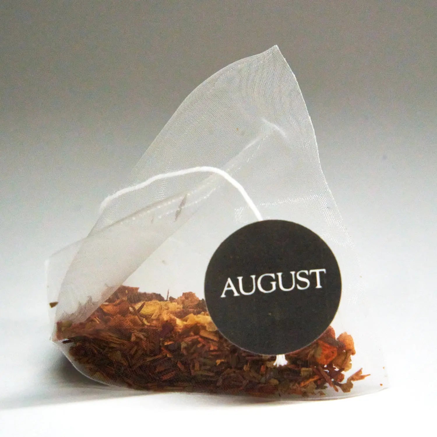 Roasted tea bag pouch filled with dried tea leaves, sealed with AUGUST logo