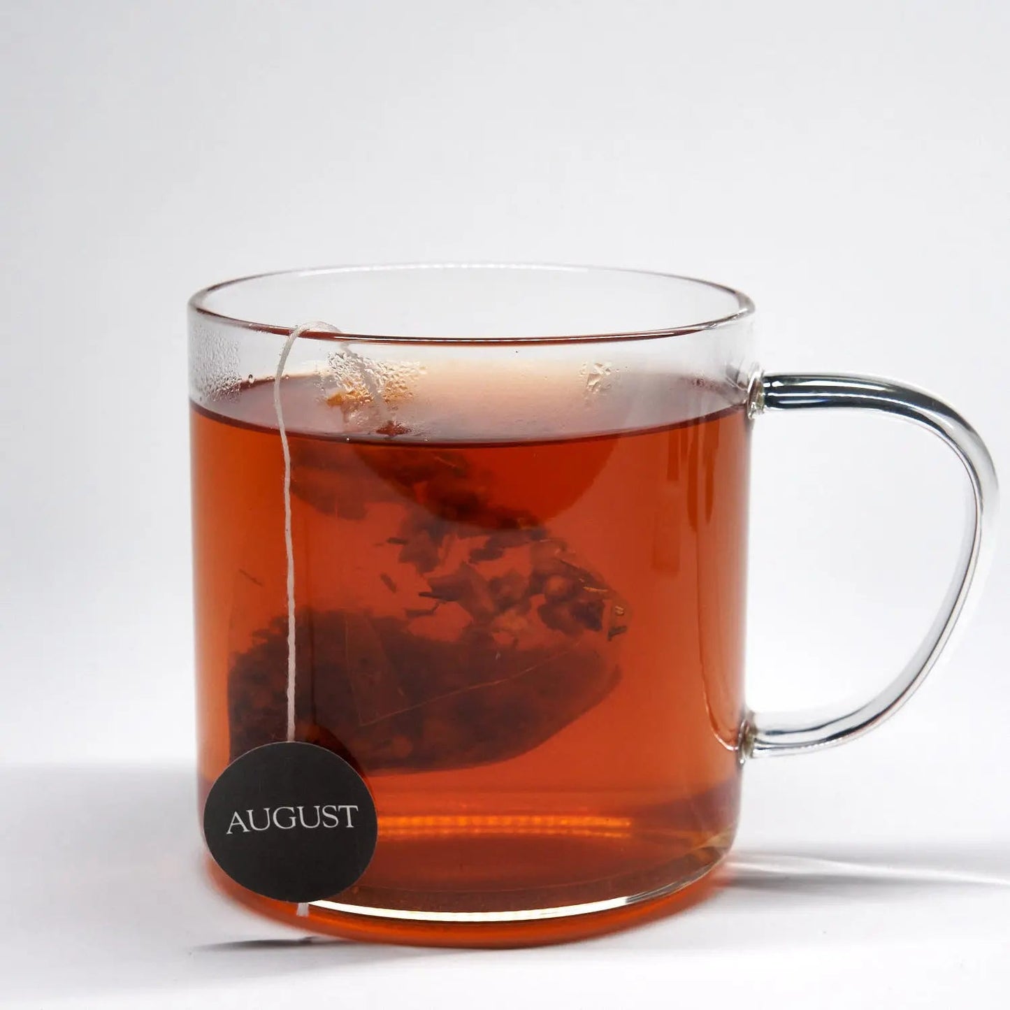 Glass mug of amber rooibos tea with AUGUST tea tag label