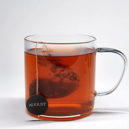 Glass mug of amber rooibos tea with AUGUST tea tag label