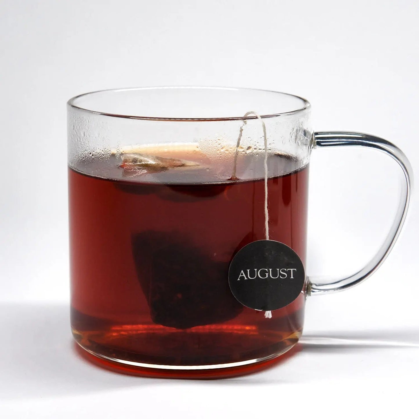 Glass mug of spiced black tea with coffee, amber color and hanging August tag