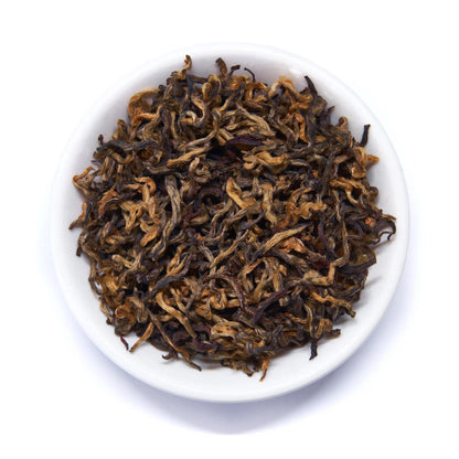 Black tea leaves, loose tea in white bowl with brown and gold tones