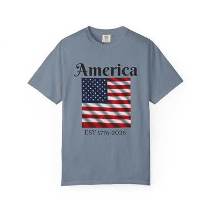 Slate blue T-shirt with “America” over US flag and “EST 1776-2026” graphic on front