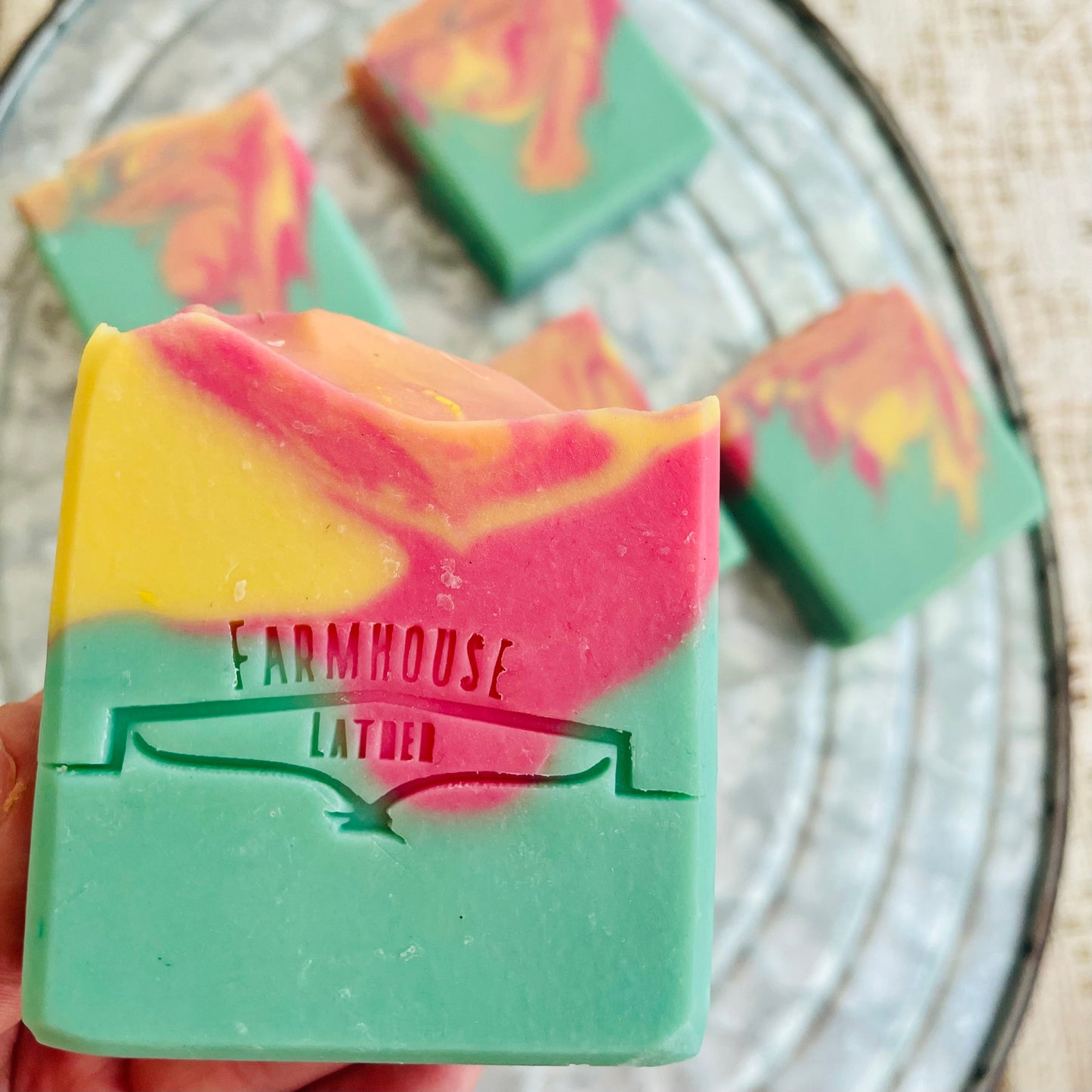 Marbled soap bar in teal, pink, and yellow with Farmhouse label, close-up corner.