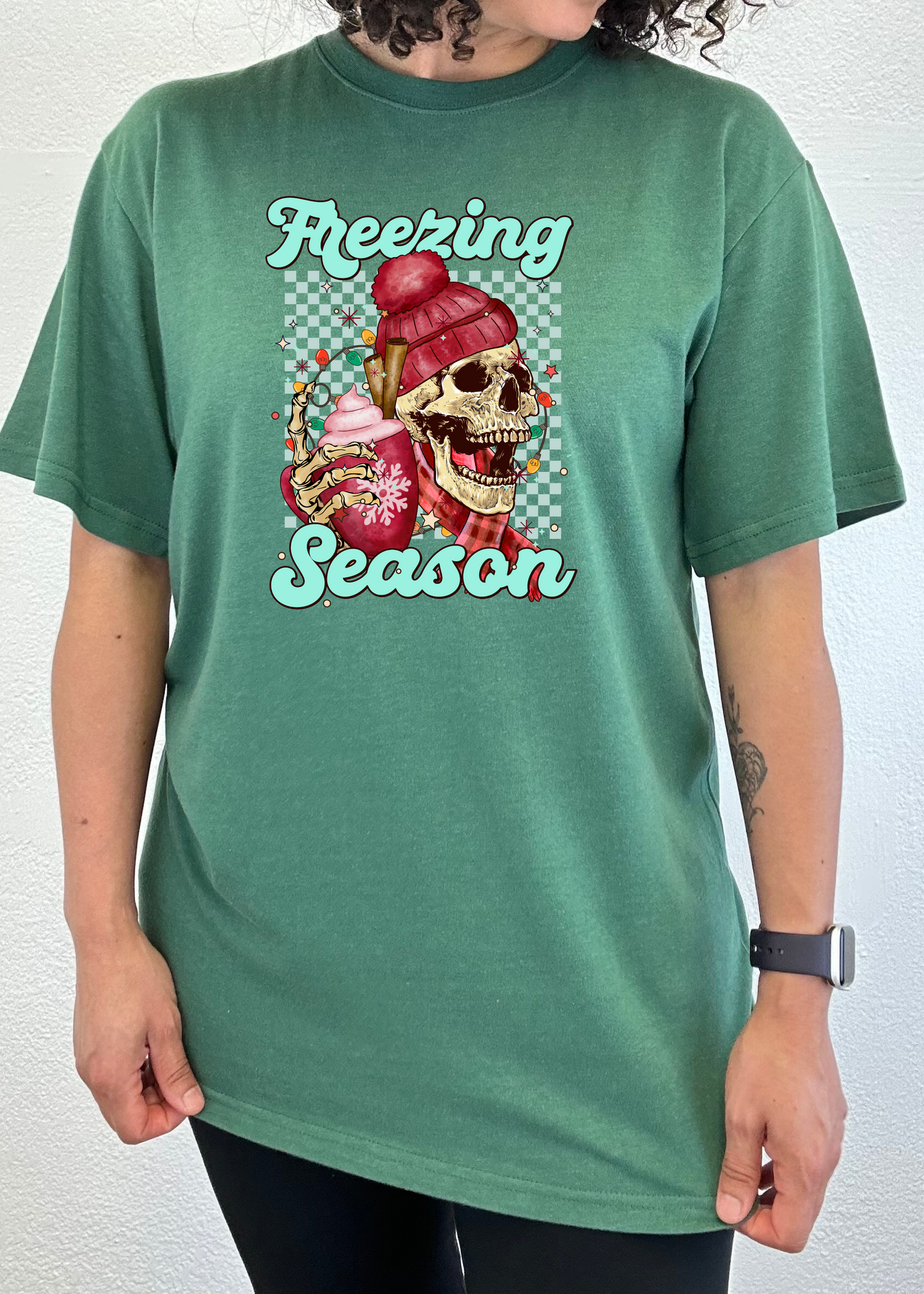 Teal green short sleeve T-shirt with “Freezing Season” skull graphic on chest.