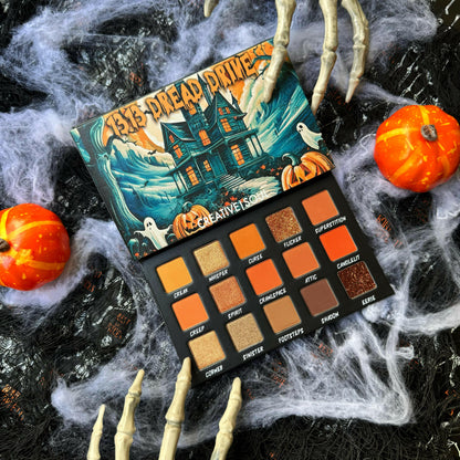 Eyeshadow palette open with 16 labeled pans showing warm orange and cool gray-brown shades