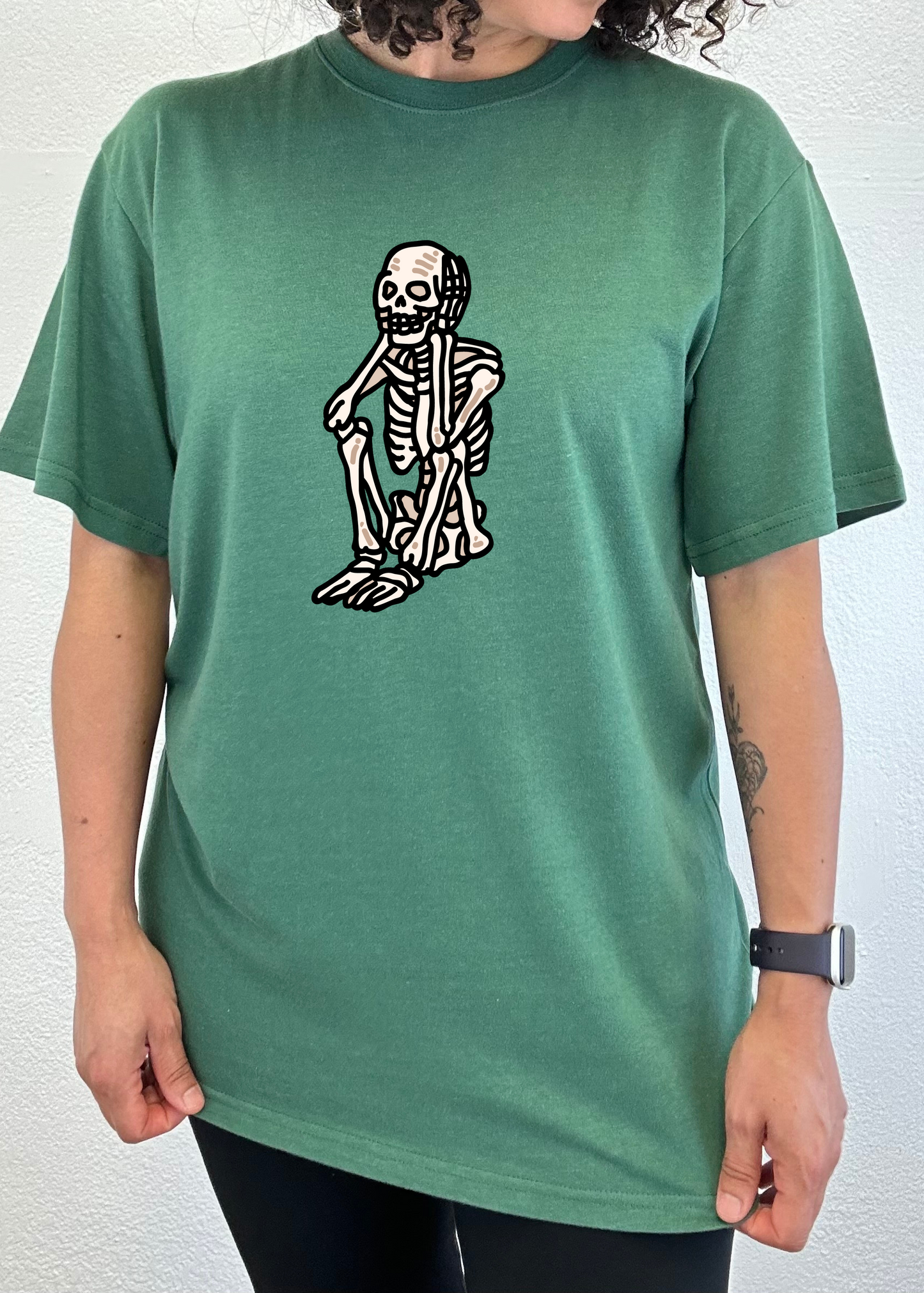 Green unisex graphic T-shirt with white skeleton standing print on chest.