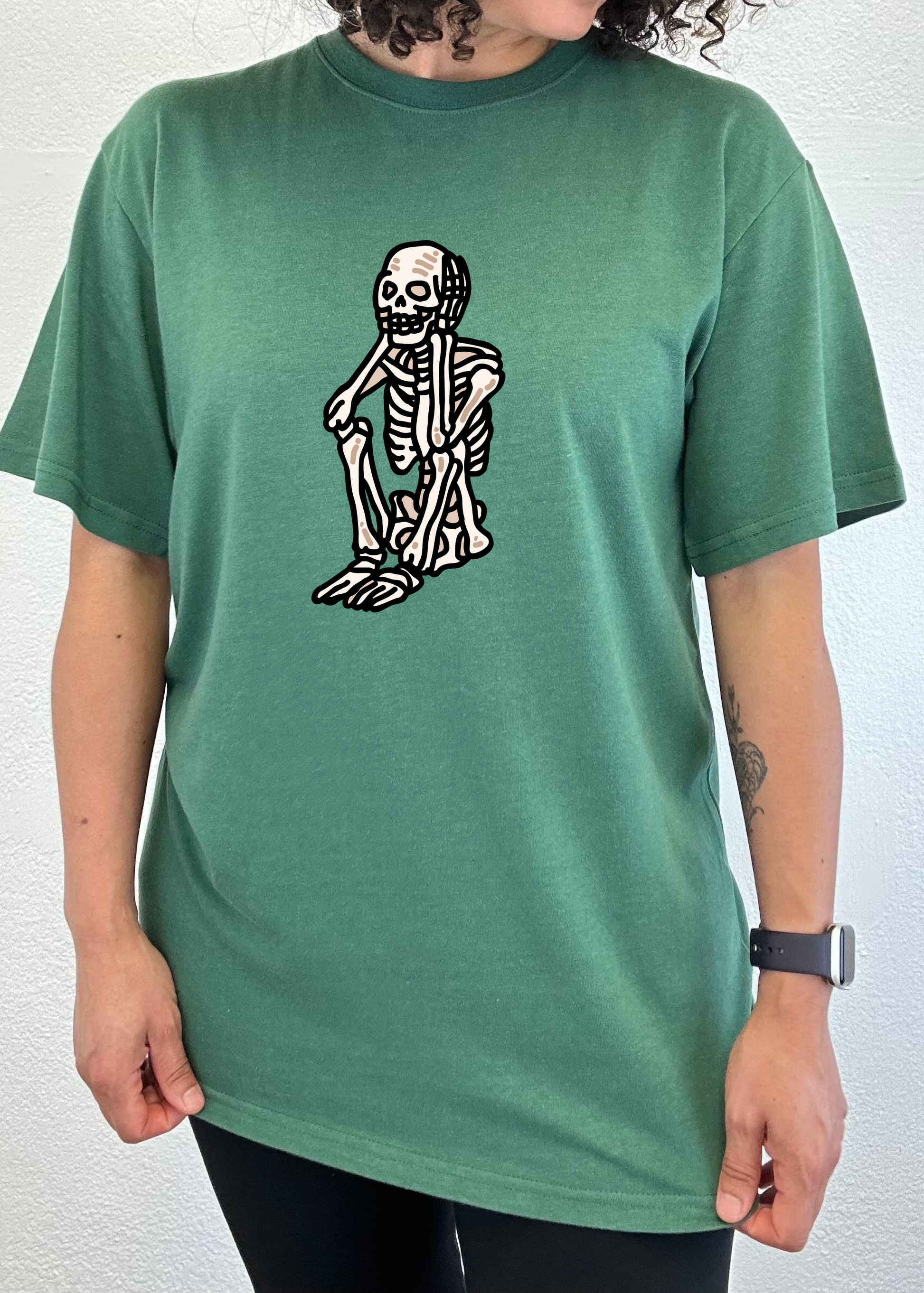 Green unisex graphic T-shirt with white skeleton standing print on chest.