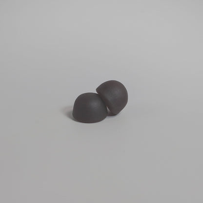 Dark mushroom gummies, two rounded pieces on a plain light gray surface