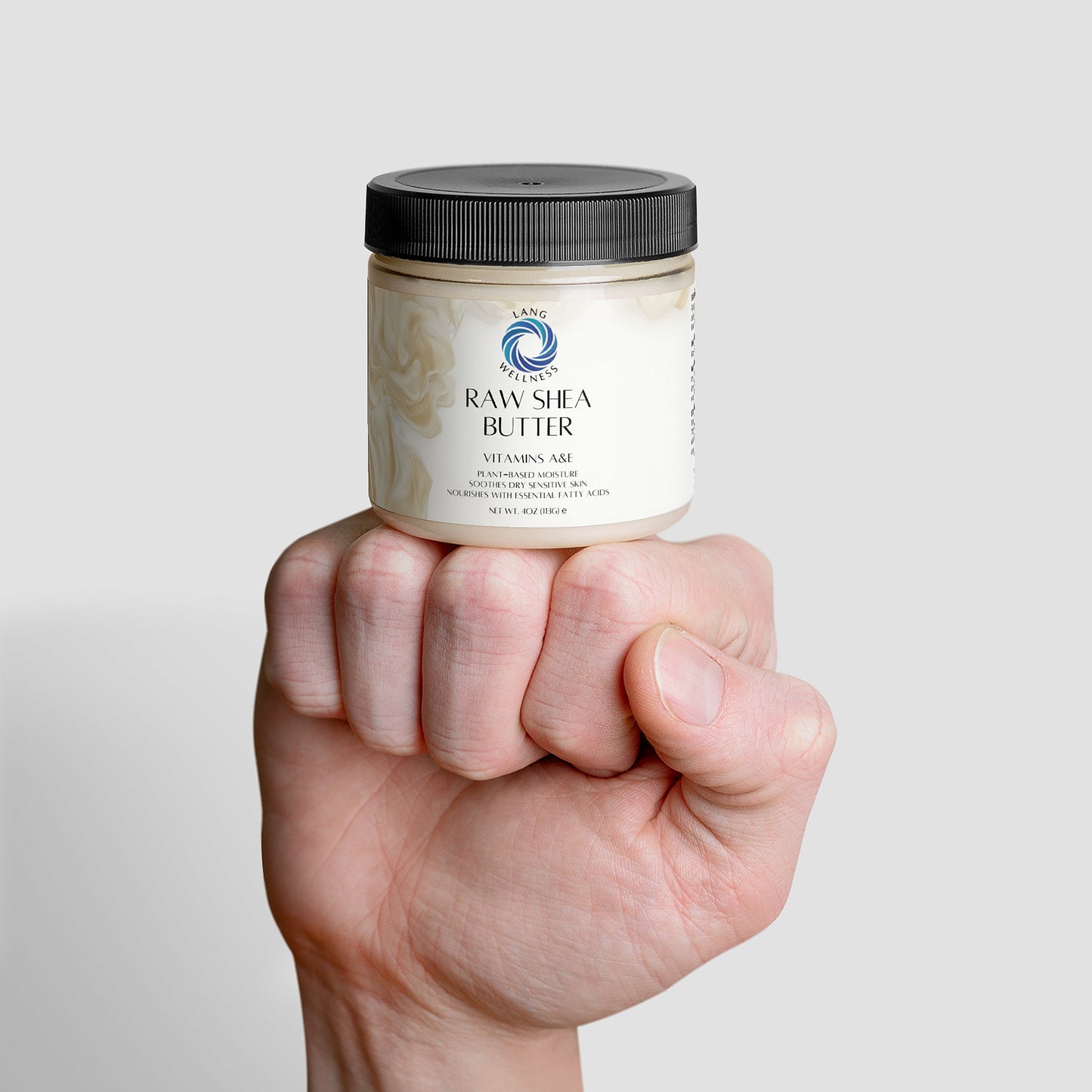 Raw shea butter jar held in hand, dark screw cap.