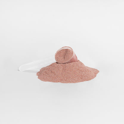 Pile of fine pinkish-red powder with a scoop utensil.