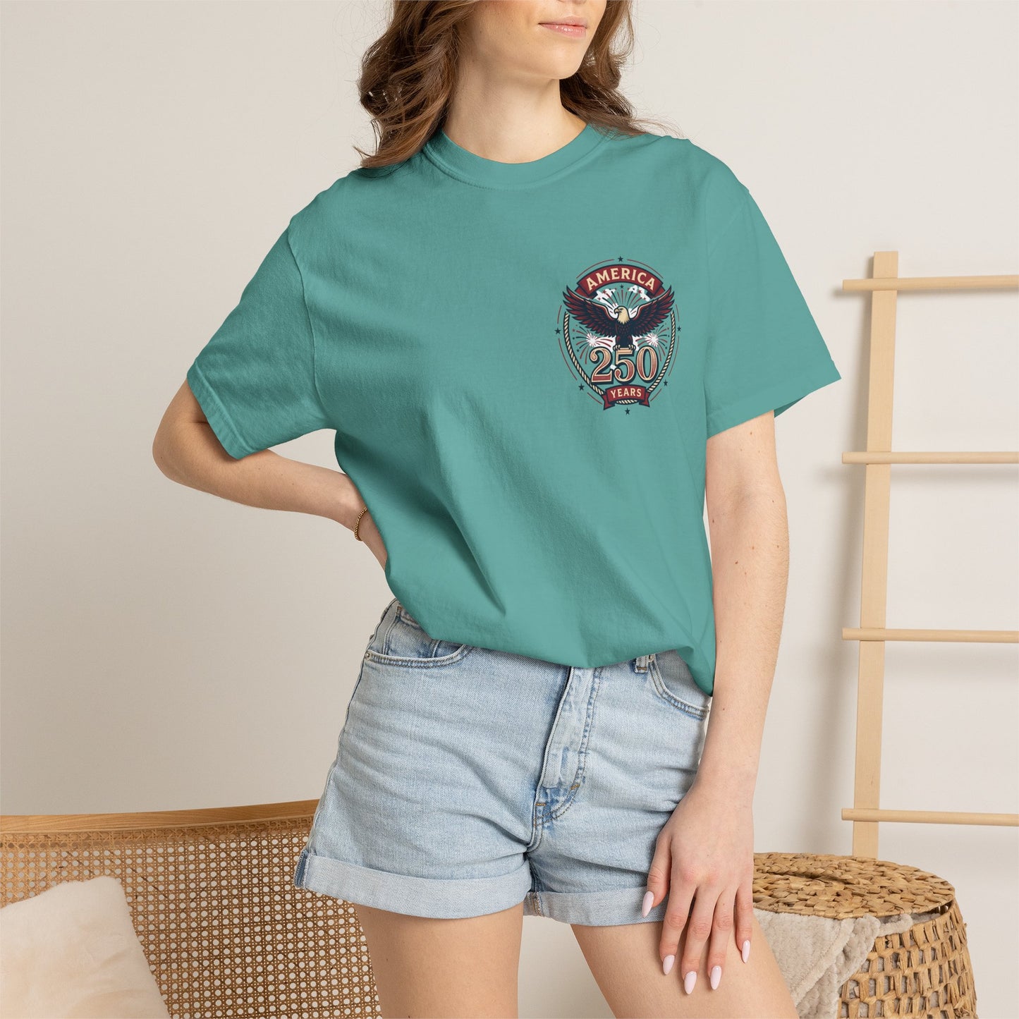 Teal T-shirt worn by model, with round “America 250 Years” emblem on chest
