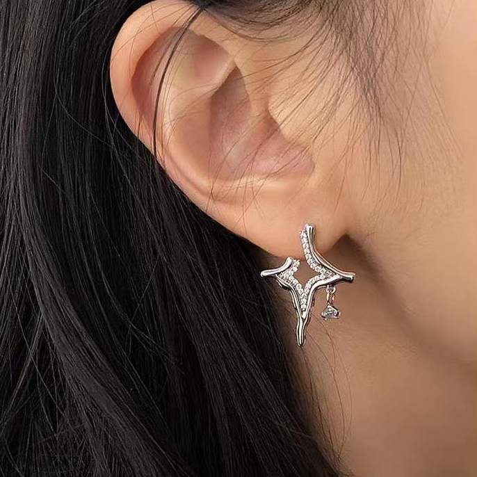 Silver rhinestone star cross earrings on ear, close-up