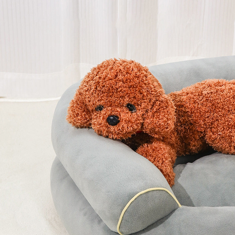 Gray pet sofa bed with rounded sides and beige piping, holding a small dog plush.