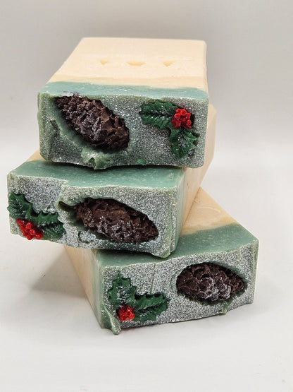 Pinecone artisan soap bars with frosted green texture, dark accents, red berries, and holly sprigs