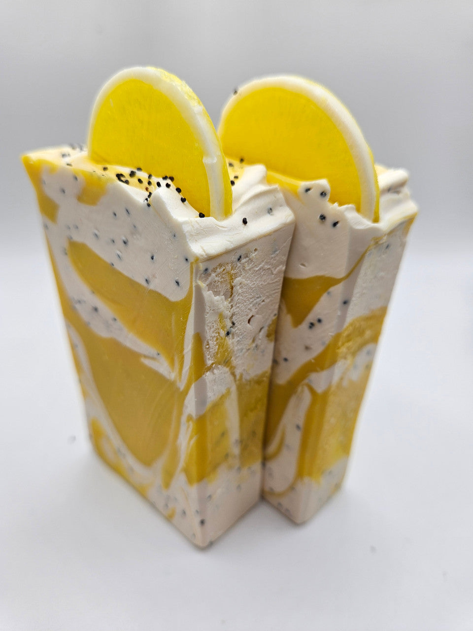 Artisan soap bars, two stacked, with yellow lemon layers, white swirls, and black specks