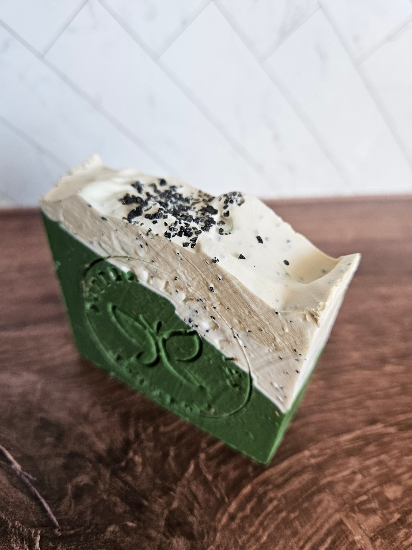 Green and white speckled soap bar with carved emblem on side, rectangular slice