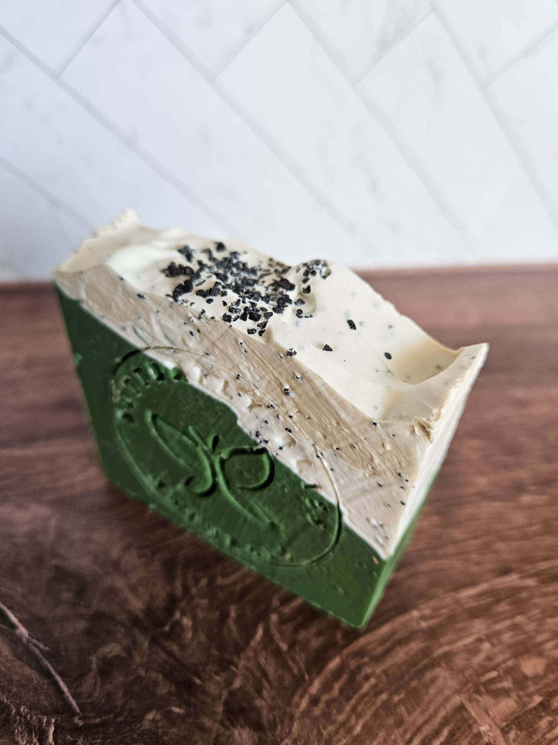 Green and white speckled soap bar with carved emblem on side, rectangular slice