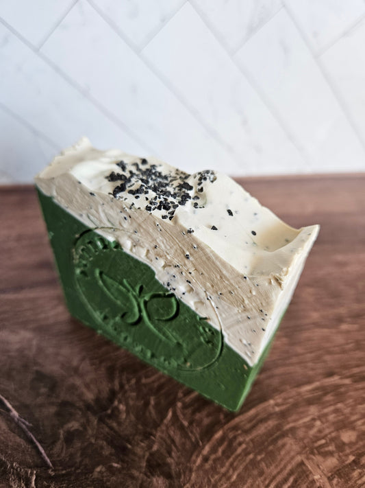 Green and white speckled soap bar with carved emblem on side, rectangular slice