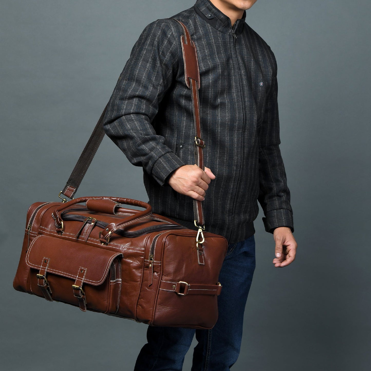 Brown leather weekender duffel on shoulder with side handle and front buckled pockets