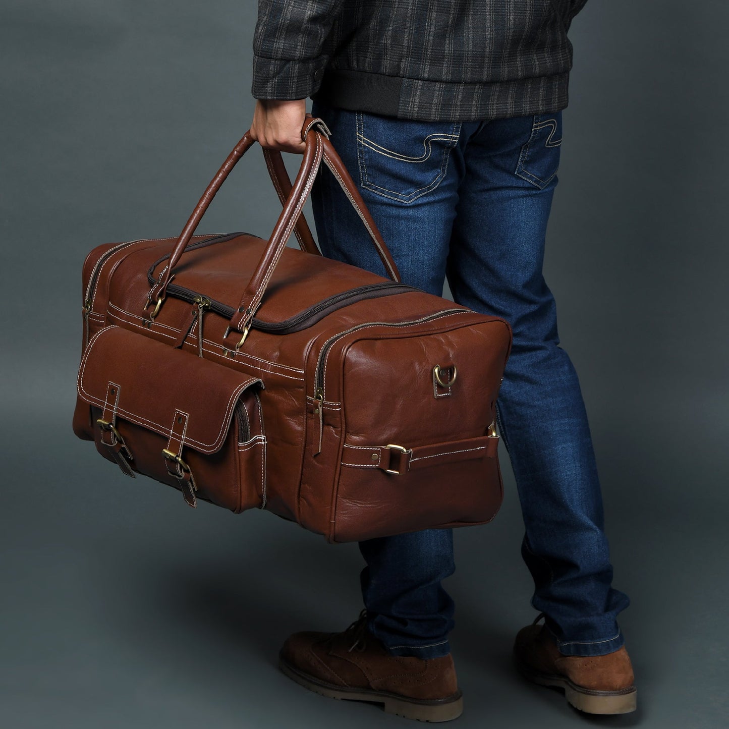 Brown leather weekender duffel held by dual handles with front flap and straps