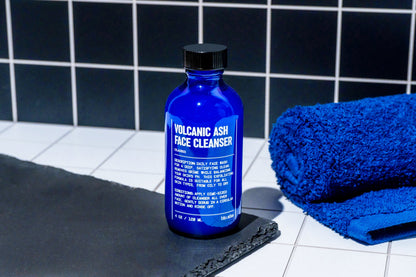 Blue face cleanser bottle with black cap beside folded towel
