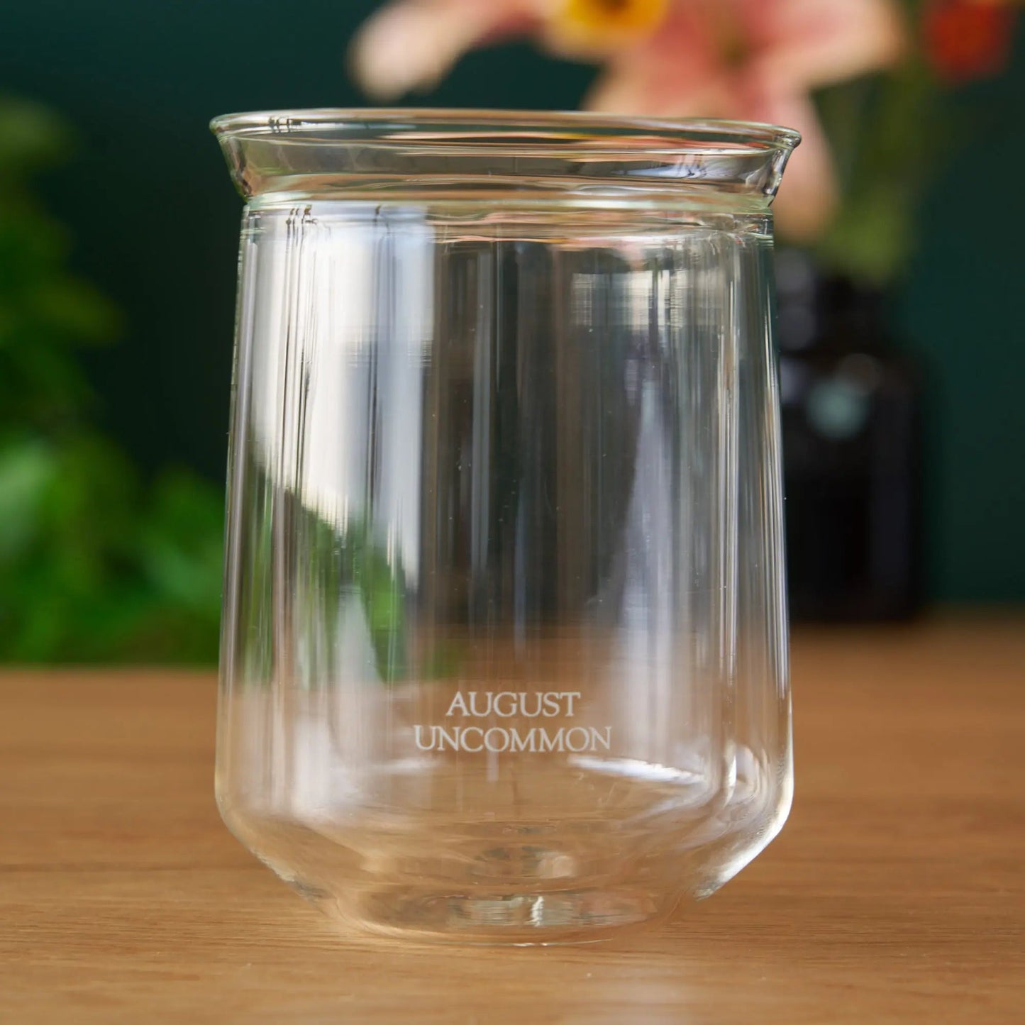 Clear tasting glass, empty; AUGUST UNCOMMON etched on the base