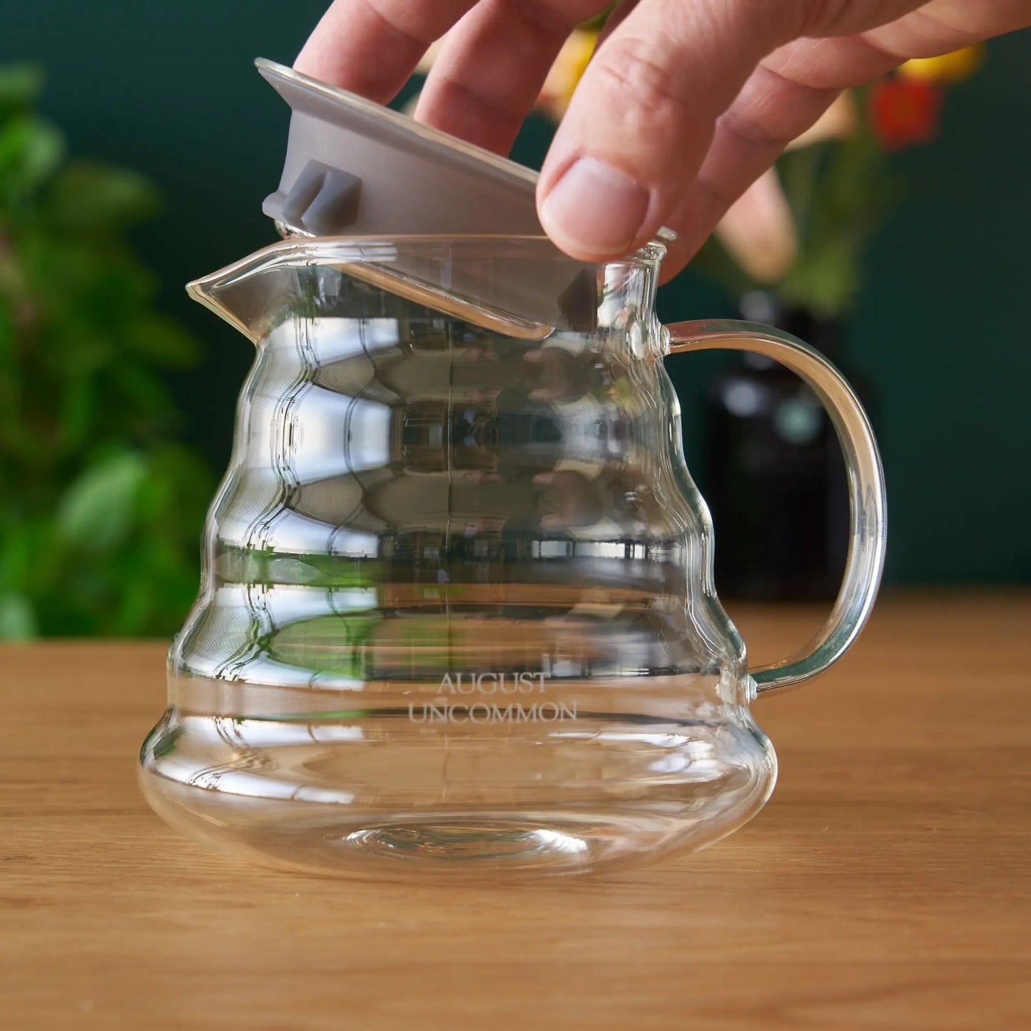 Two-cup glass teapot with lid, clear handle, hand holding the top.